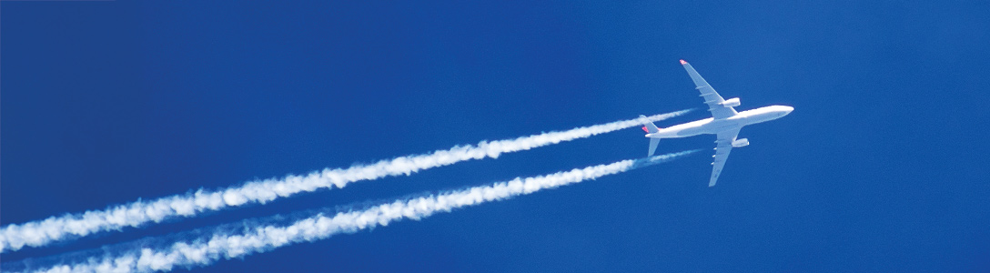 Airplane flying through sky with condensation trail under a dark blue sky Airplane flying through sky with condensation trail under a dark blue sky